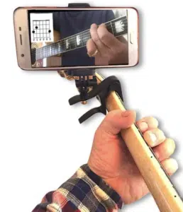 Close-up of a person holding a guitar neck with a capo and smartphone attached, displaying a chord diagram on the screen—a perfect gift idea for musicians seeking inspiration.